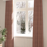 A large, sunny window with long curtains in a fern leaf print on a dark red field.