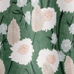 Draped fabric in a playful floral print in shades of white, pink and green on a light green field.