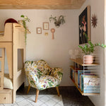 A children's bunk bed with a stuffed armchair in a large-scale botanical print in pink, yellow, green and cream.