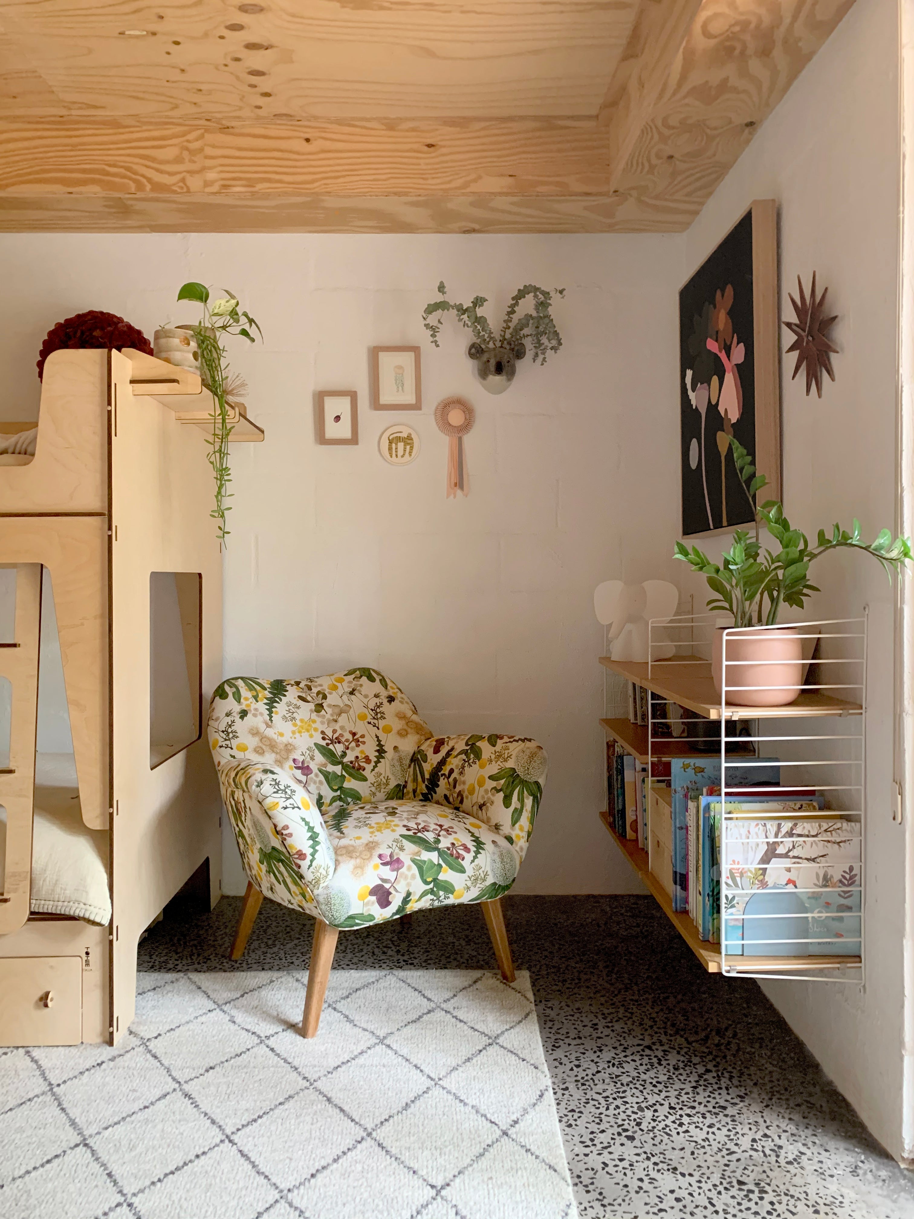 A children's bunk bed with a stuffed armchair in a large-scale botanical print in pink, yellow, green and cream.