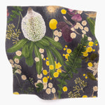 Square fabric swatch in a large-scale botanical print in shades of pink, yellow and green on a navy field.
