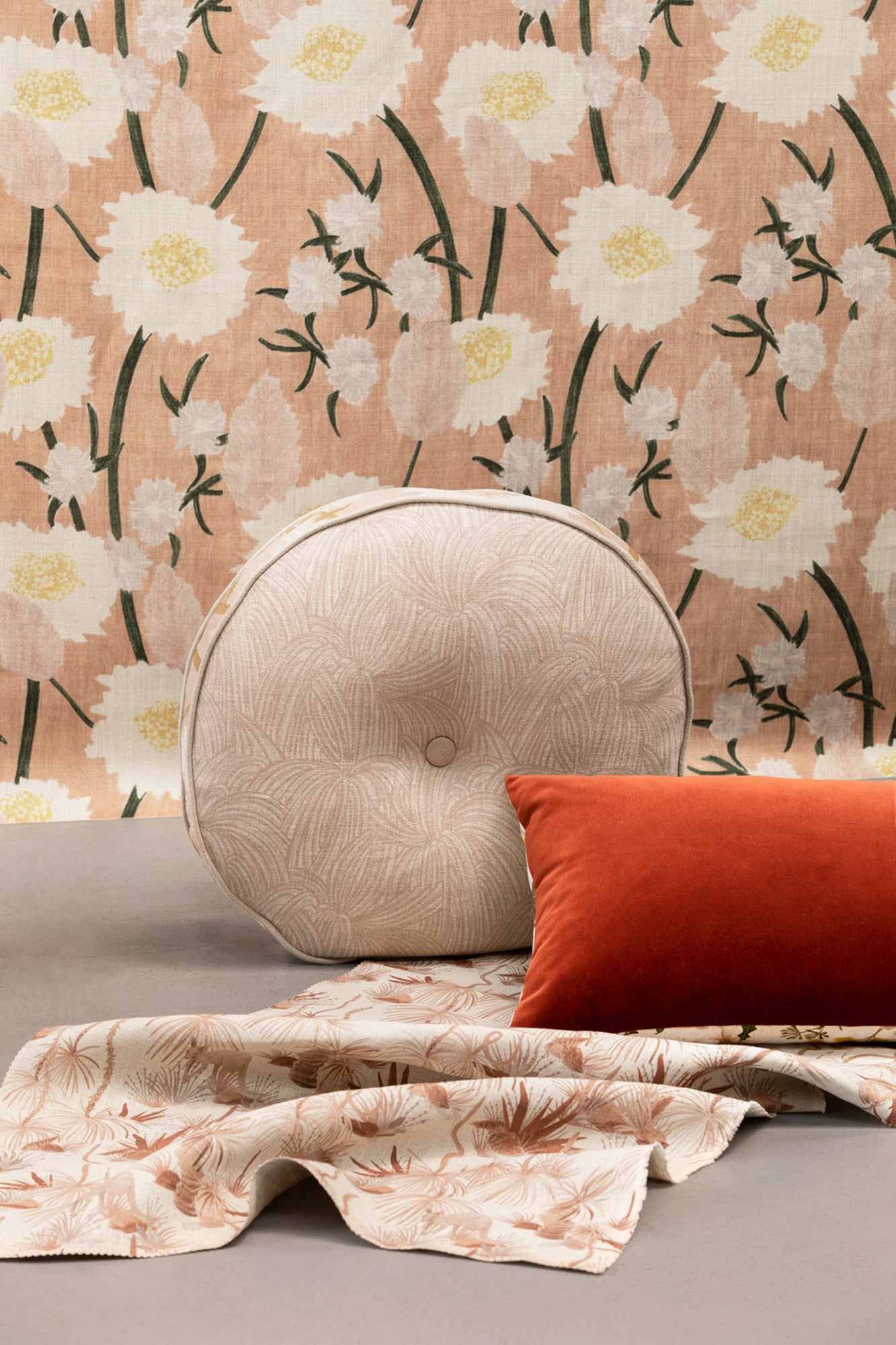 A tableau of arranged throw pillows and fabric yardage in tan, red and various floral prints.