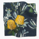 Square fabric swatch in a photorealistic floral print in shades of yellow, white and green on a navy field.