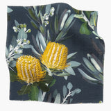 Square fabric swatch in a photorealistic floral print in shades of yellow, white and green on a navy field.