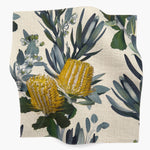 Square fabric swatch in a photorealistic floral print in shades of yellow, white and green on a cream field.