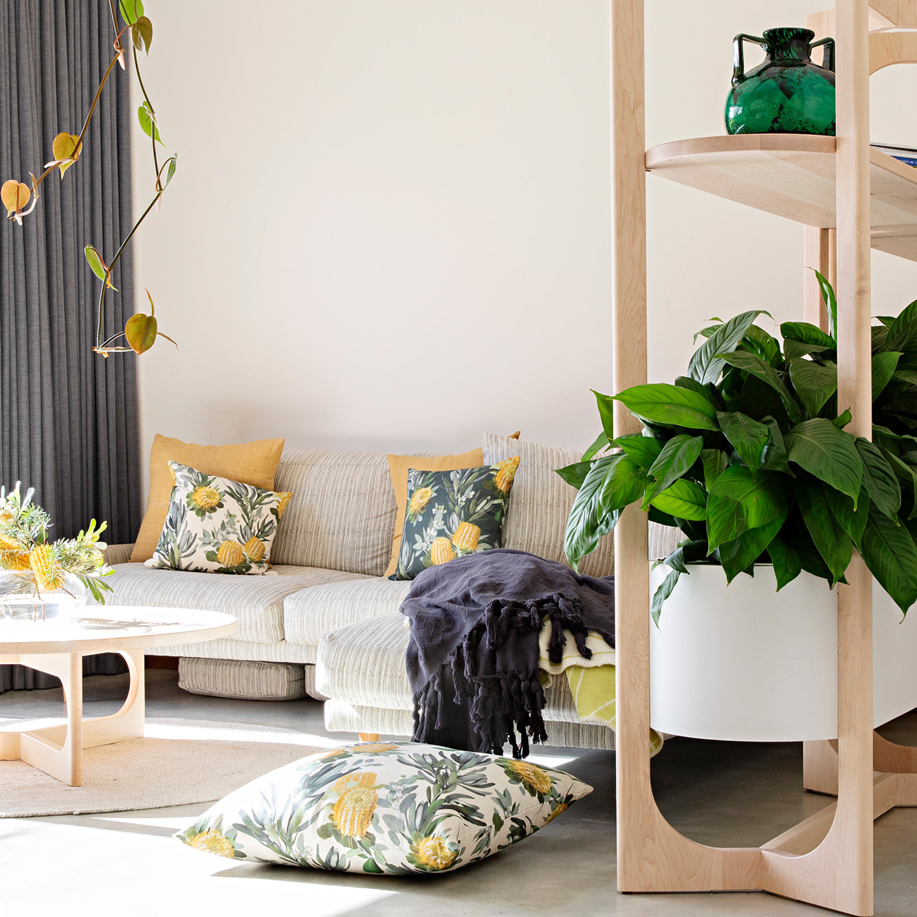 Plant-filled living room with a low sofa covered in throw pillows in photorealistic floral prints.