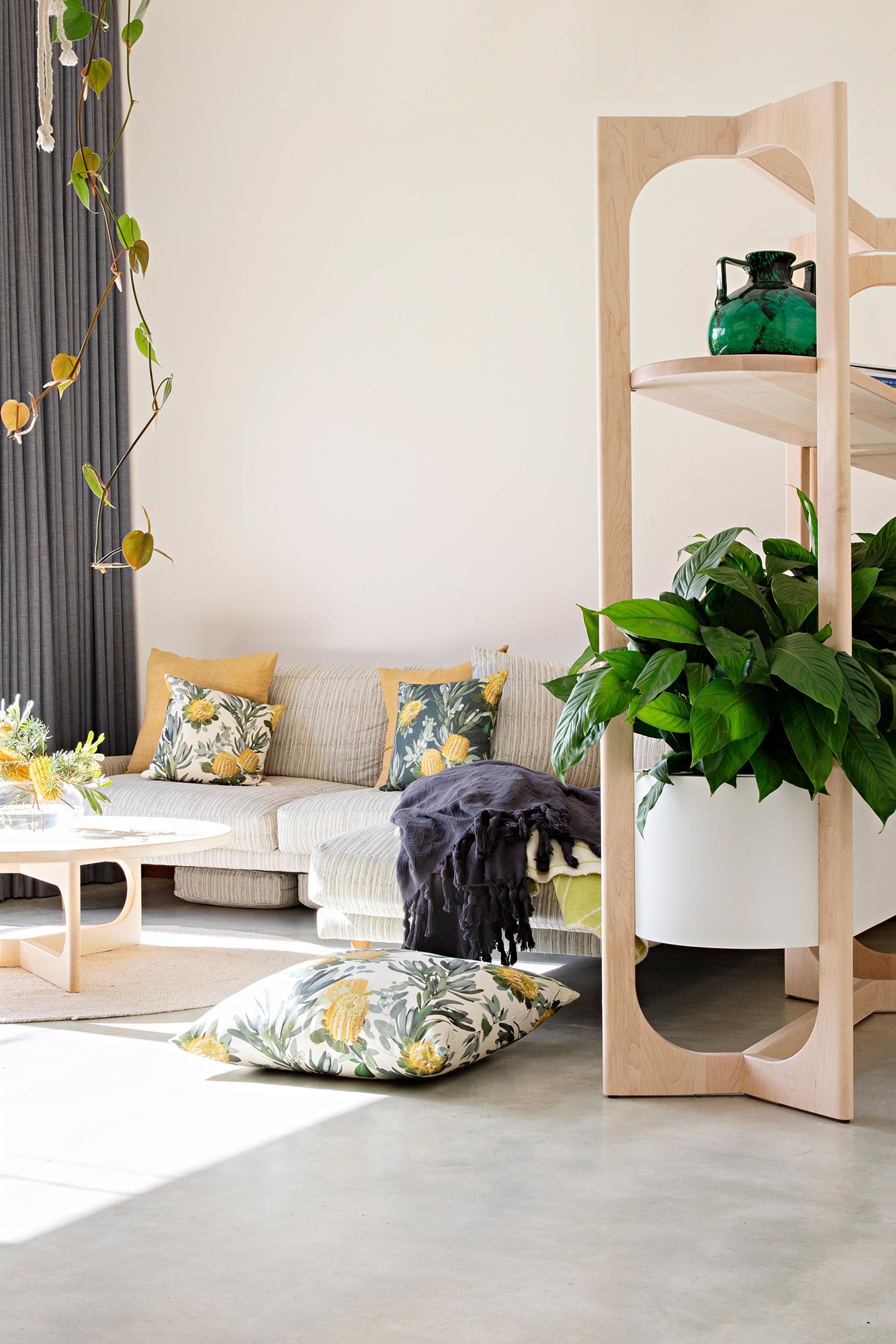 Plant-filled living room with a low sofa covered in throw pillows in photorealistic floral prints.