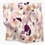 Square fabric swatch in an abstract shape print in shades of purple, maroon and orange on a cream field.