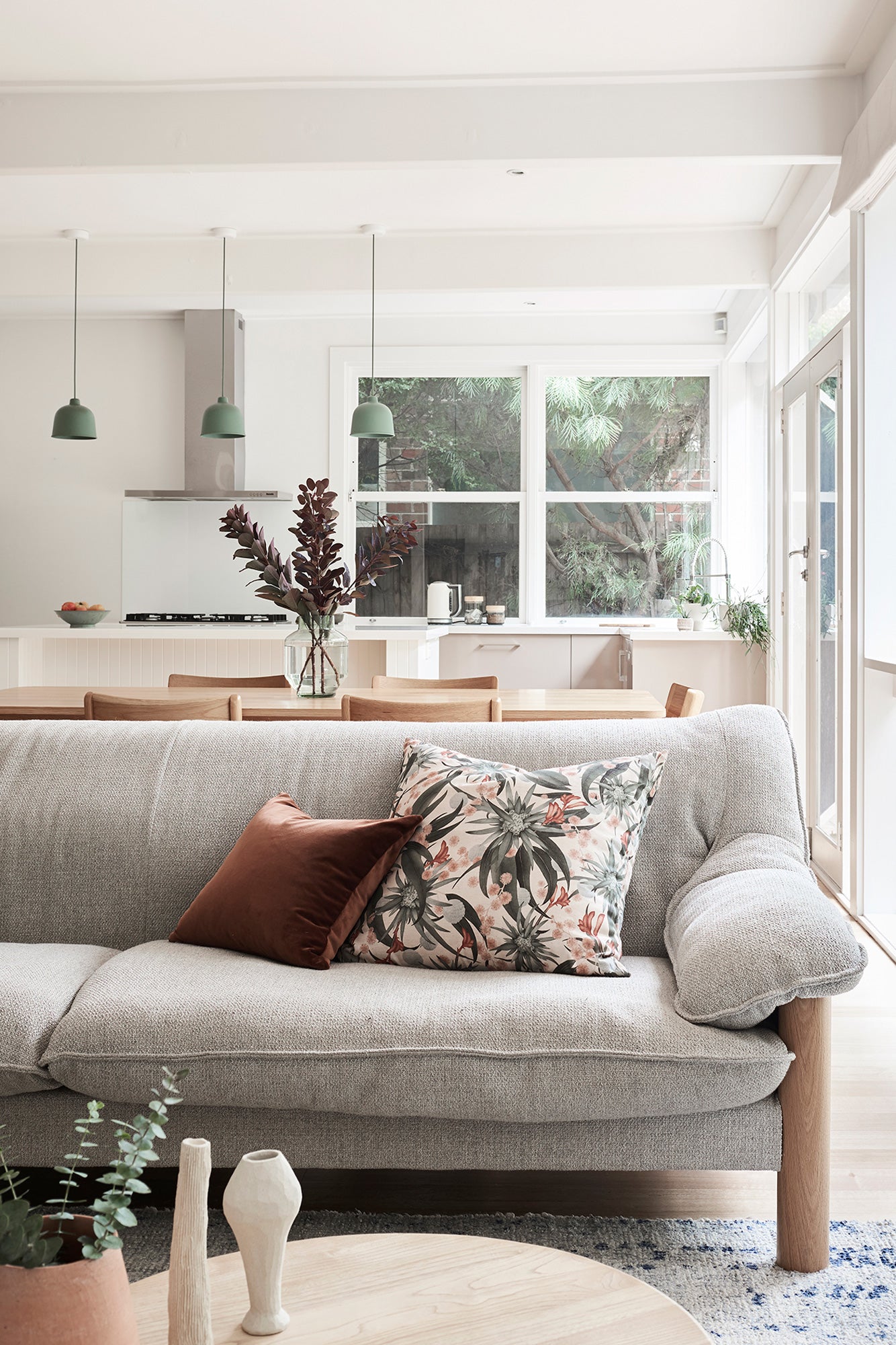 Modernist living and dining space with a gray couch topped with a throw pillow in a photorealistic floral print.