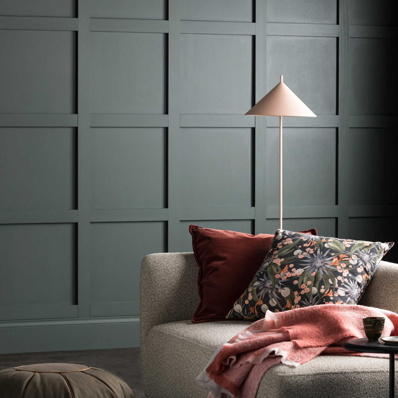 A moody living tableau with dark green walls and a couch stacked in pink and floral throw pillows.