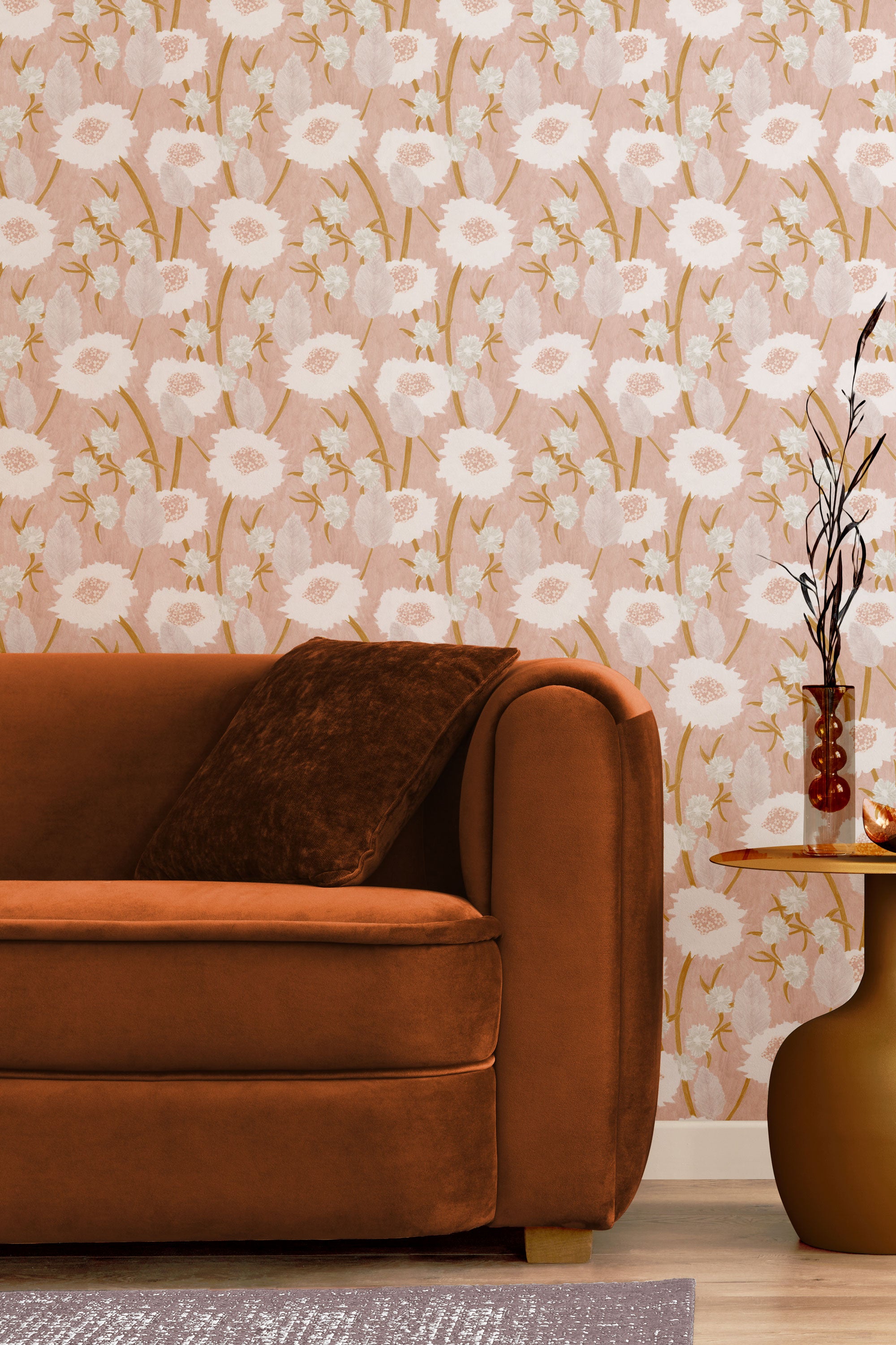 A couch and end table stand in front of a wall papered in a playful floral print in pink, white and tan.