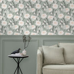 A couch and end table stand in front of a wall papered in a playful floral print in white, pink, gray and green.