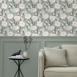 A couch and end table stand in front of a wall papered in a playful floral print in white, pink, gray and green.