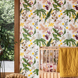 A maximalist baby nursery with a wall papered in a large-scale botanical print in pink, yellow, green and cream.