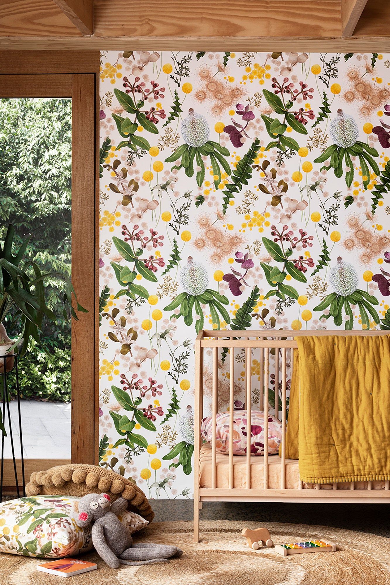 A maximalist baby nursery with a wall papered in a large-scale botanical print in pink, yellow, green and cream.