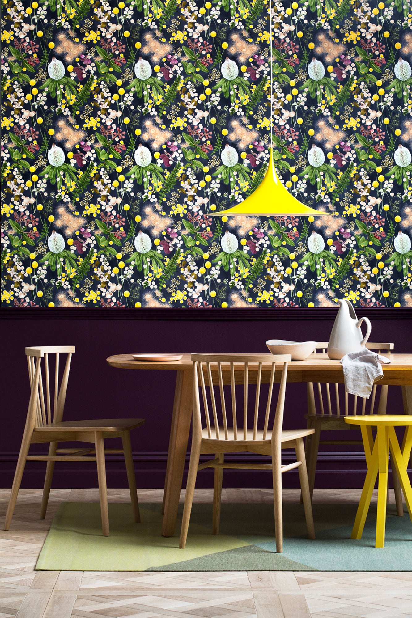 A maximalist dining room with a wall papered in a large-scale botanical print in pink, yellow, green and navy.