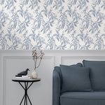 A maximalist living room with a wall papered in a painterly leaf print in blue-gray on a white field.