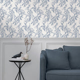 A maximalist living room with a wall papered in a painterly leaf print in blue-gray on a white field.