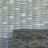 A metal end table stands in front of a wall papered in an undulating ribbon pattern in charcoal.