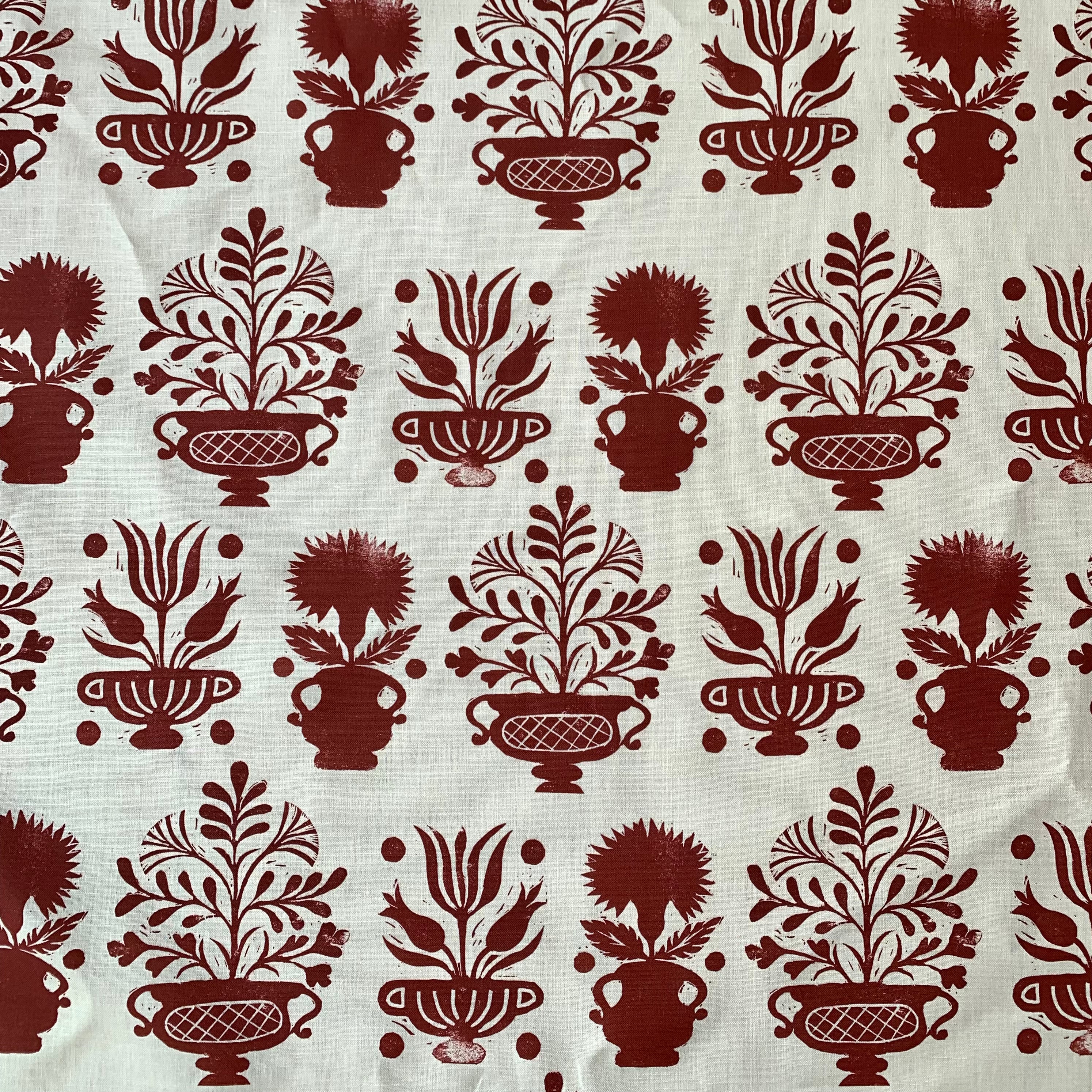 Detail of fabric in a repeating vase and plant print in rust on a white field.