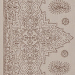 Detail of fabric in a dense paisley border print in brown on a tan field.