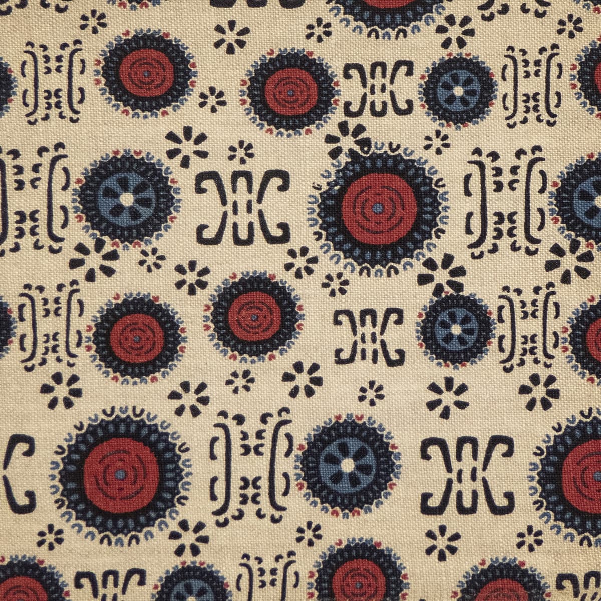 Detail of fabric in a repeating geometric shape print in shades of red, navy and black on a tan field.