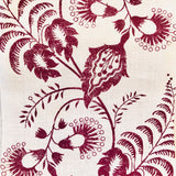 Detail of fabric in a floral trellis print in dark red on a cream field.