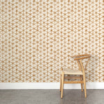 A wooden chair stands in front of a wall papered in a painterly lattice print in brown on a cream field.