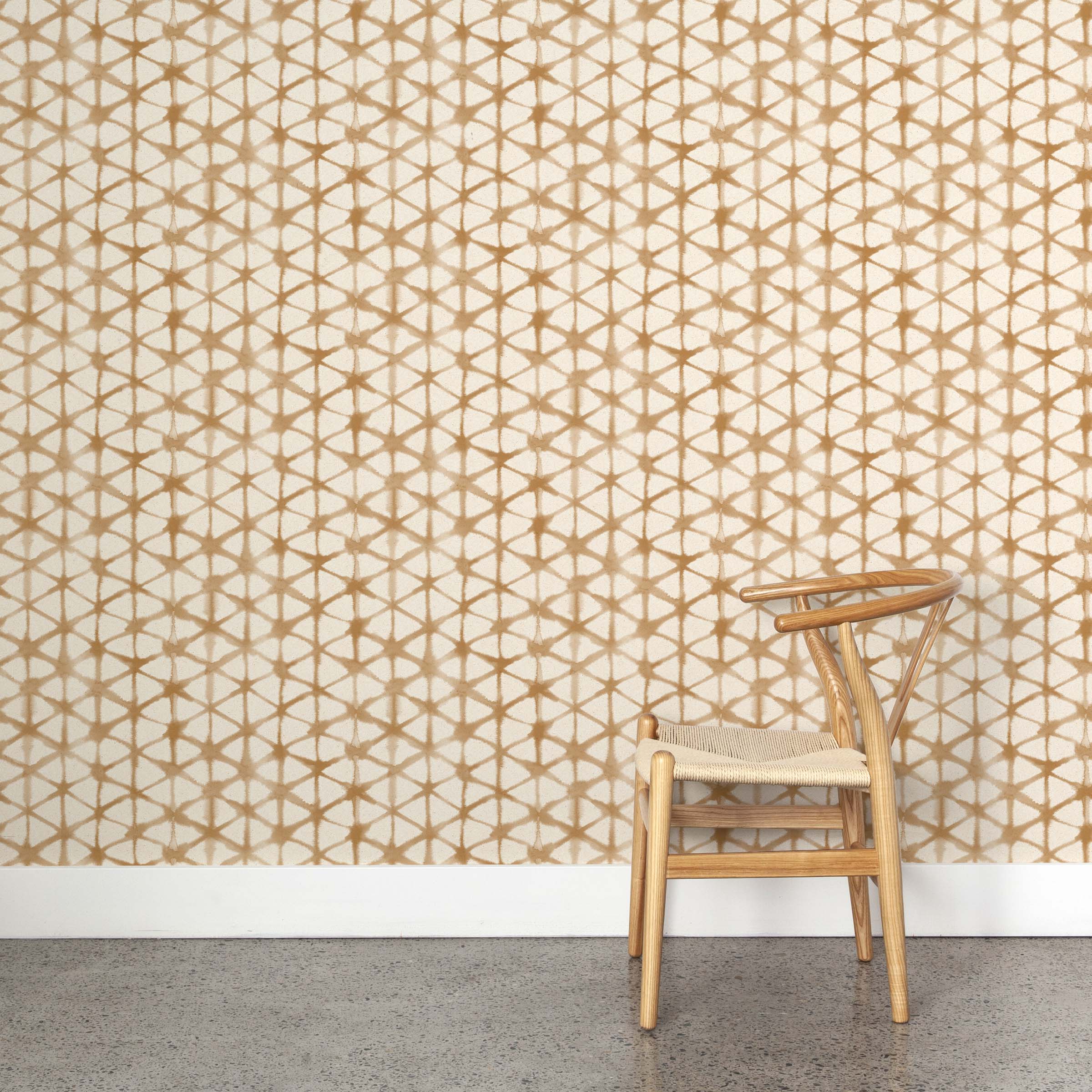 A wooden chair stands in front of a wall papered in a painterly lattice print in brown on a cream field.