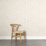 A wooden chair stands in front of a wall papered in a painterly lattice print in tan on a cream field.