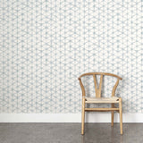 A wooden chair stands in front of a wall papered in a painterly lattice print in light blue on a cream field.