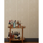 A bronze bar cart in front of a wall papered in a repeating mosaic stripe print in shades of brown and gray-blue on a tan field.