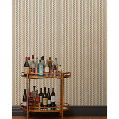 A bronze bar cart in front of a wall papered in a repeating mosaic stripe print in shades of brown and gray-blue on a tan field.