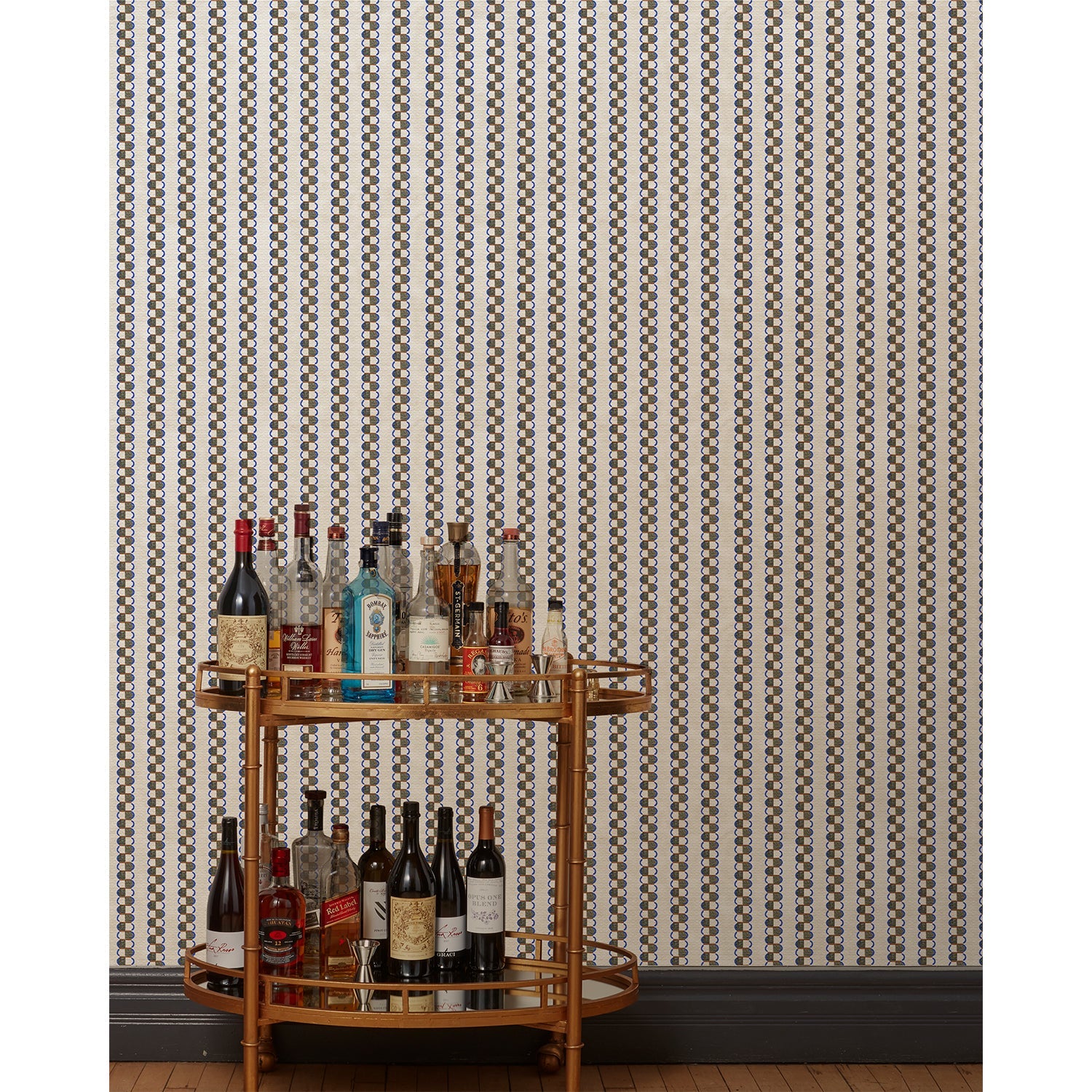 A bronze bar cart in front of a wall papered in a repeating mosaic stripe print in shades of blue, rust and gray on a cream field.