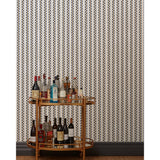 A bronze bar cart in front of a wall papered in a repeating mosaic stripe print in shades of blue, rust and gray on a cream field.