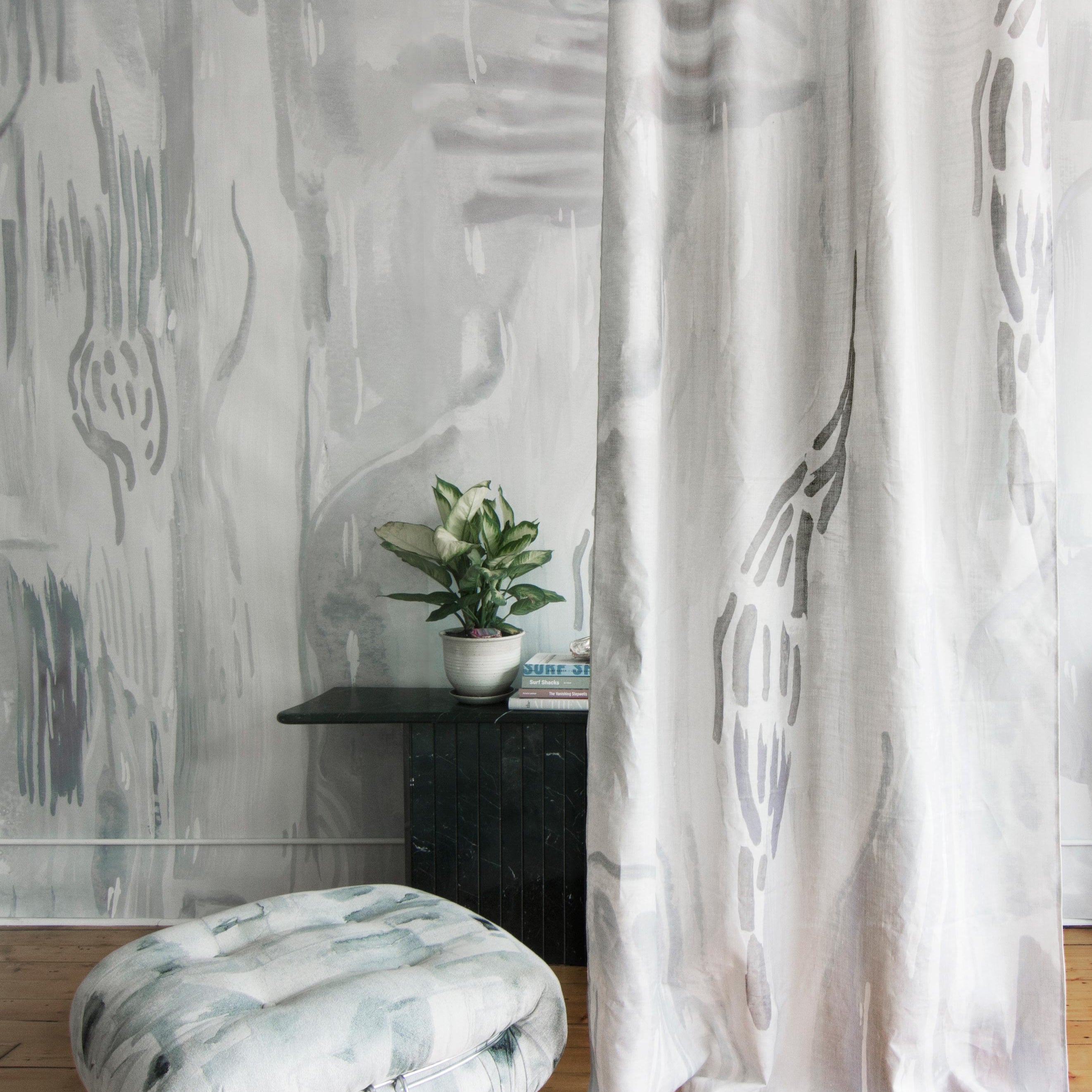 A floor pillow and curtain, both upholstered in coordinating abstract paint prints in shades of gray and blue on white fields.