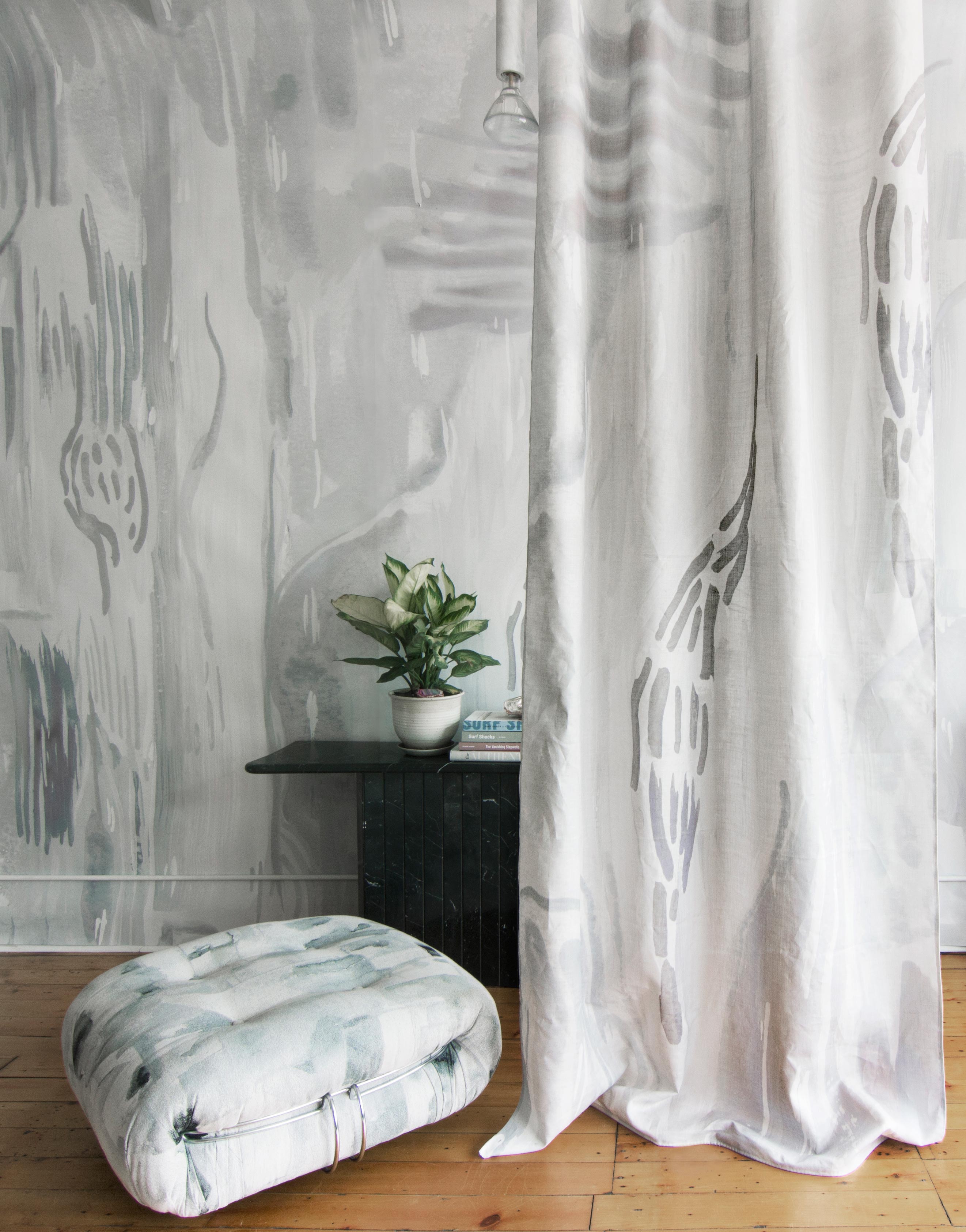 A floor pillow and curtain, both upholstered in coordinating abstract paint prints in shades of gray and blue on white fields.