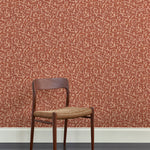 A wooden dining chair against a botanical lace pattern wallpaper in tonal shades rust red.