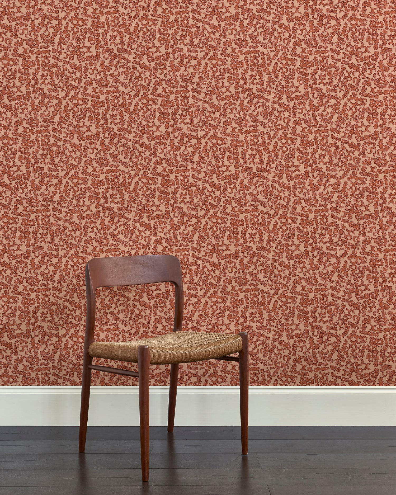 A wooden dining chair against a botanical lace pattern wallpaper in tonal shades rust red.