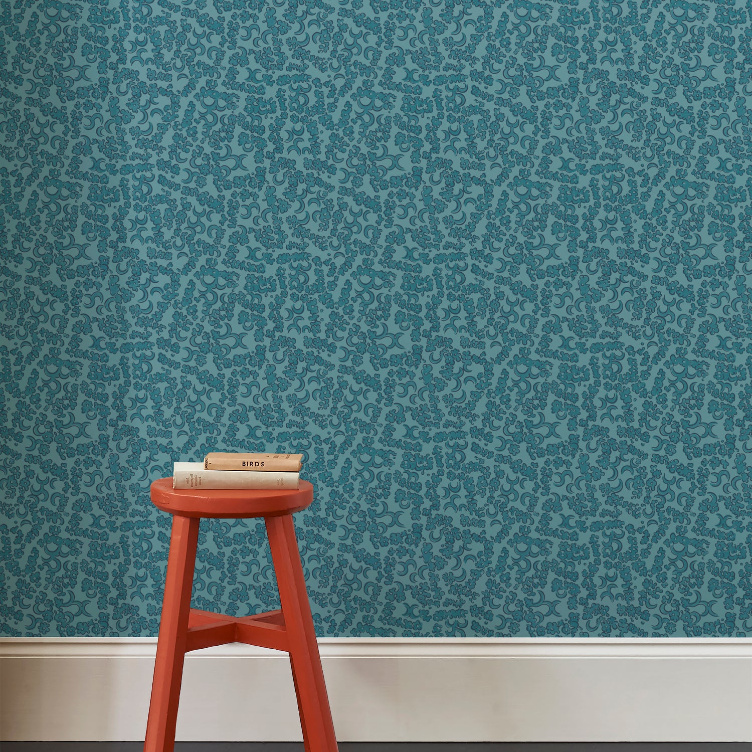 A red wooden stool against wallpaper in botanical lace pattern in tonal shades of marine blue.