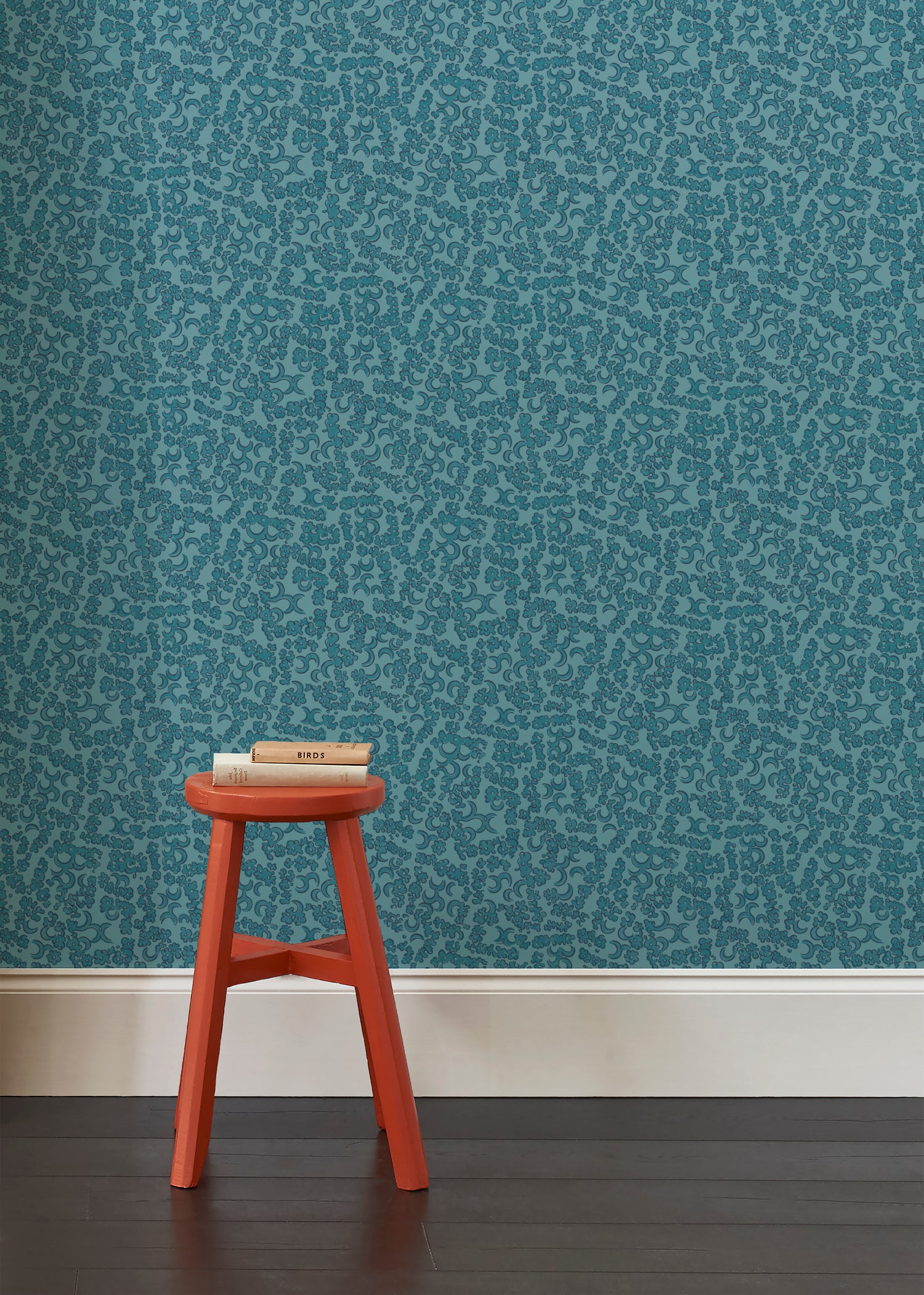 A red wooden stool against wallpaper in botanical lace pattern in tonal shades of marine blue.