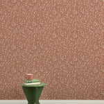 A green wooden stool with books and a mug against botanical lace patterned wallpaper in terracotta pink.