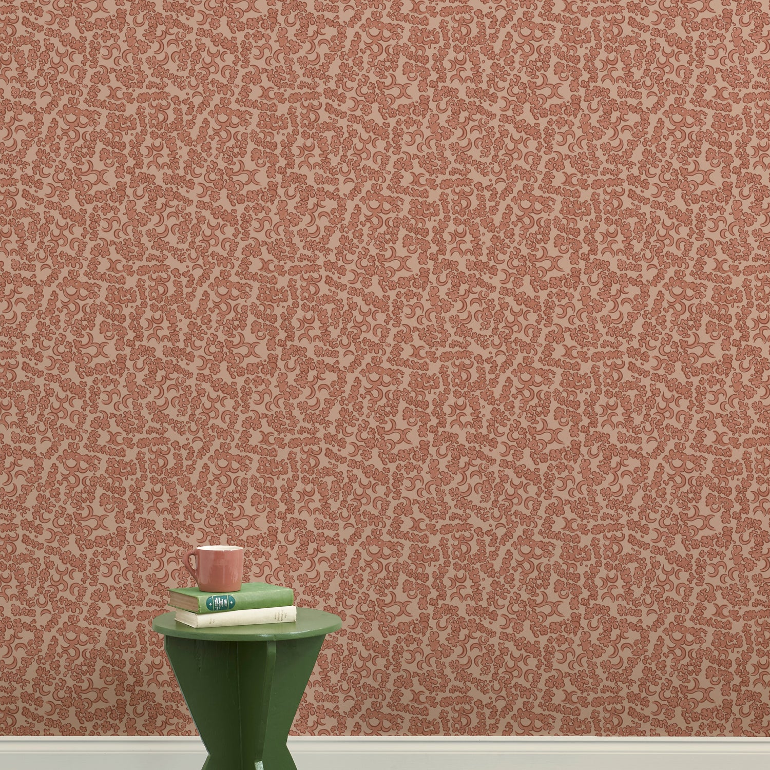 A green wooden stool with books and a mug against botanical lace patterned wallpaper in terracotta pink.