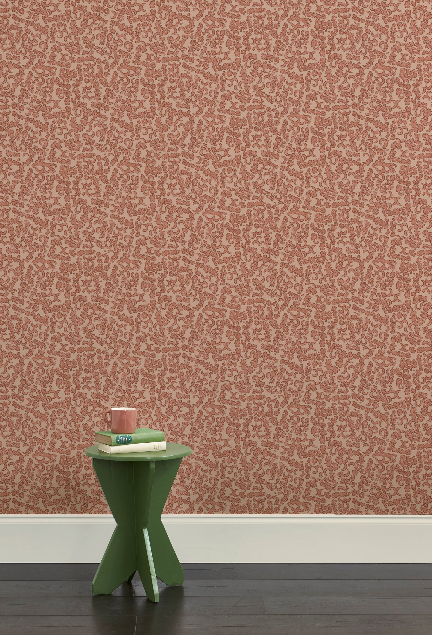 A green wooden stool with books and a mug against botanical lace patterned wallpaper in terracotta pink.