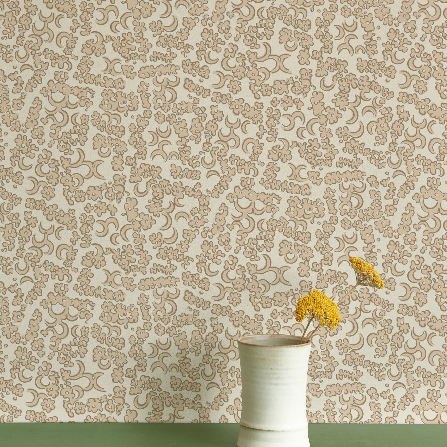 A ceramic vase with yellow wildflowers against wallpaper in a botanical lace pattern in tonal shades of light taupe and ivory.