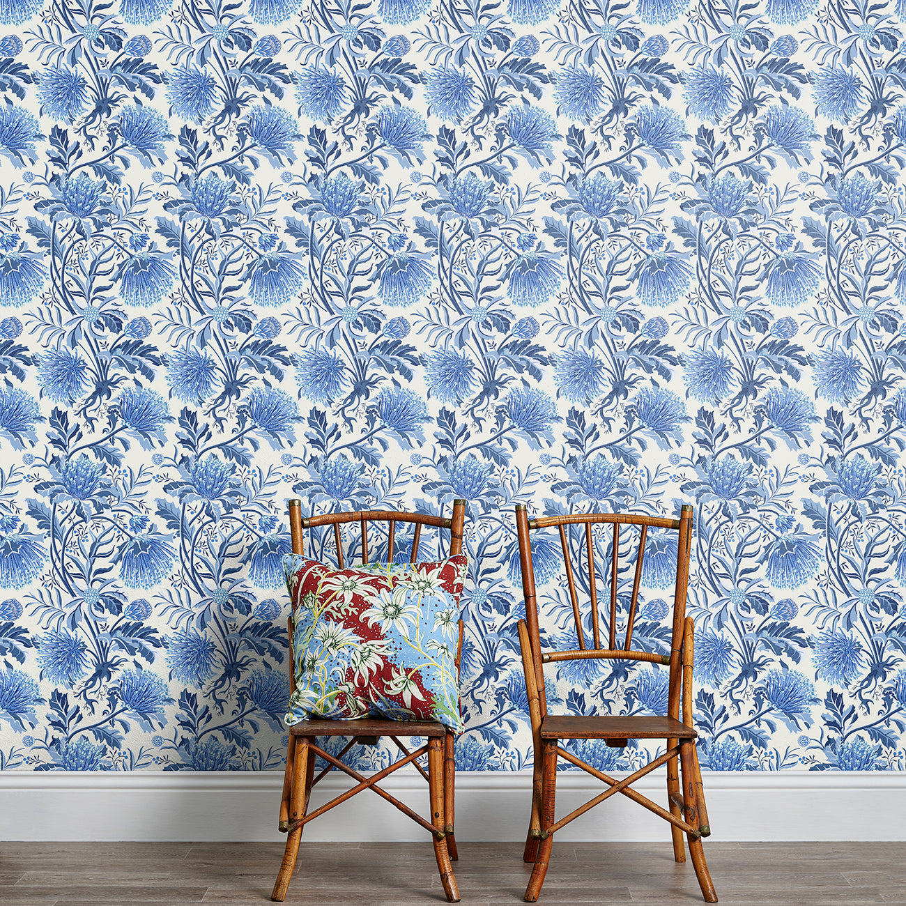 Two wooden chairs stand in front of a wall papered in a dense floral print in blue, navy and white.