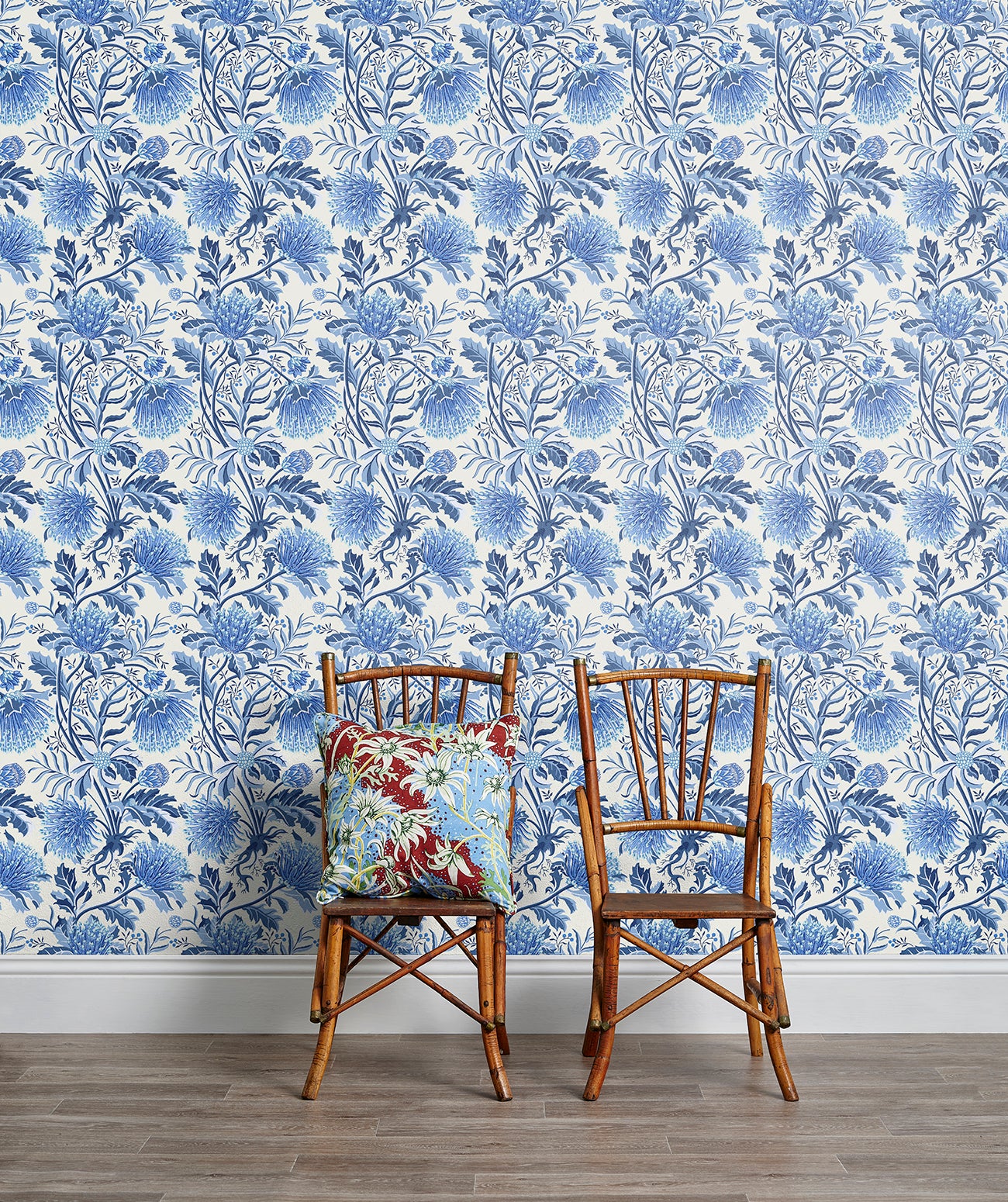 Two wooden chairs stand in front of a wall papered in a dense floral print in blue, navy and white.