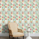 Armchair and end table in front of a wall papered in a dense floral print in pink, yellow, green and white.