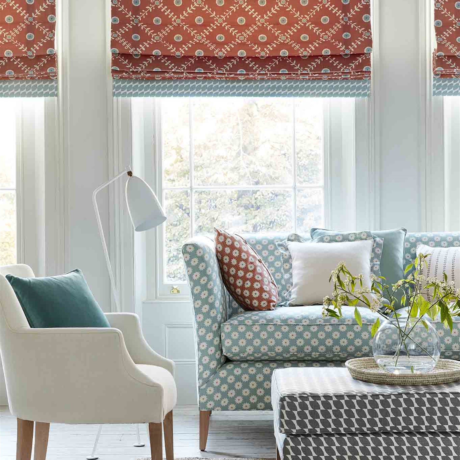 A cozy living space with an armchair, ottoman and curtains all upholstered in different colorways of the same floral print.