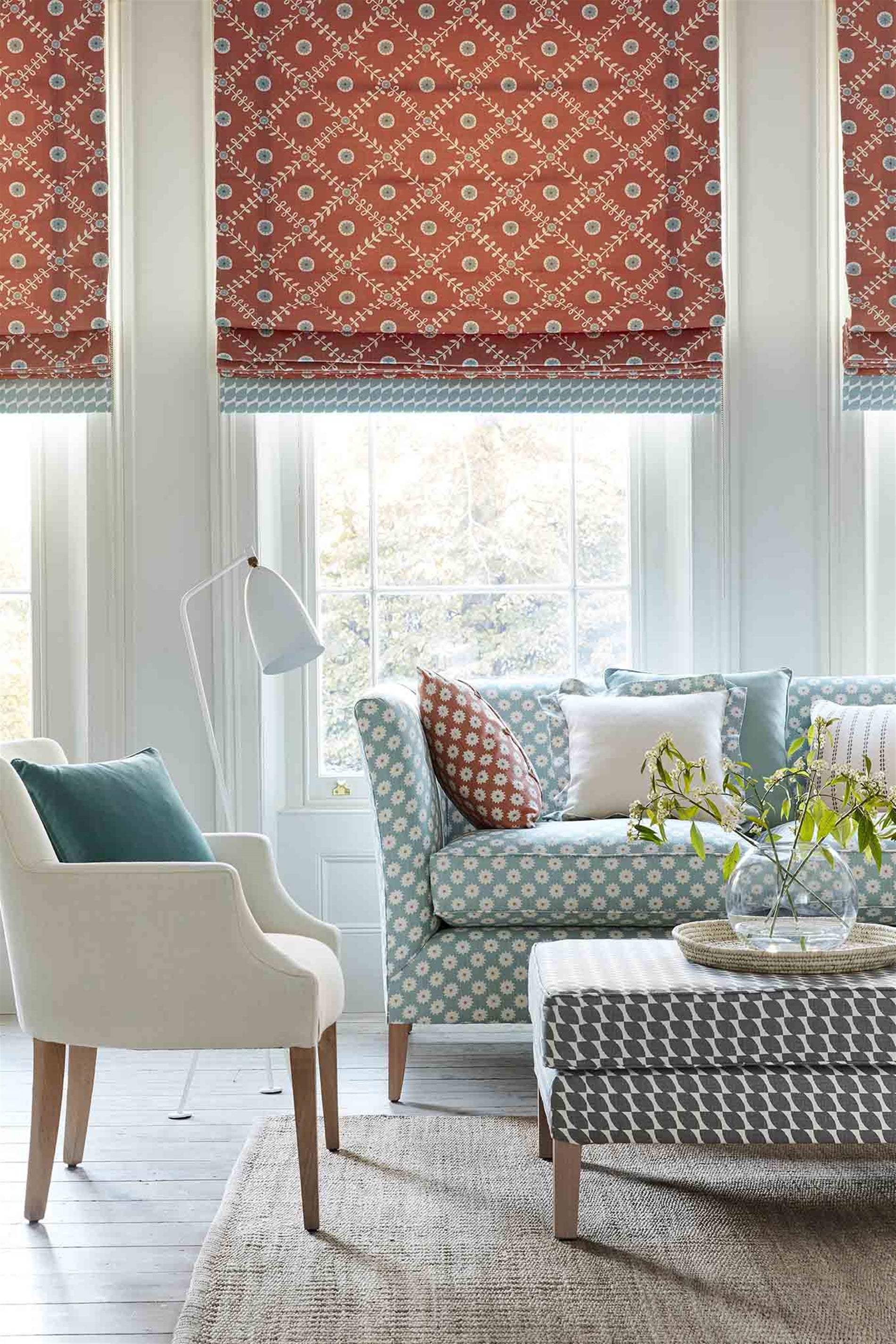 A cozy living space with an armchair, ottoman and curtains all upholstered in different colorways of the same floral print.